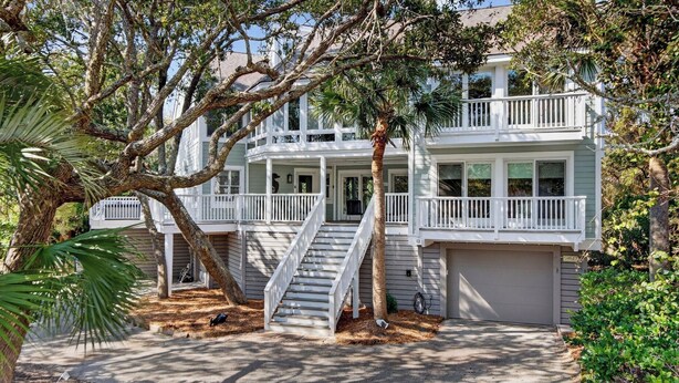 A two-story house with a porch, a staircase, and a garage. - 12 Dunecrest Lane by Avantstay 2 Mins to Beach w/ Pool & BBQ (Isle of Palms)