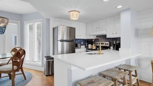 Una cocina moderna con armarios blancos, un refrigerador de acero inoxidable, una estufa a gas y una isla con taburetes.
