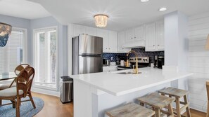A modern kitchen with white cabinetry, a stainless steel refrigerator, a gas stove, and a bar island with stools.