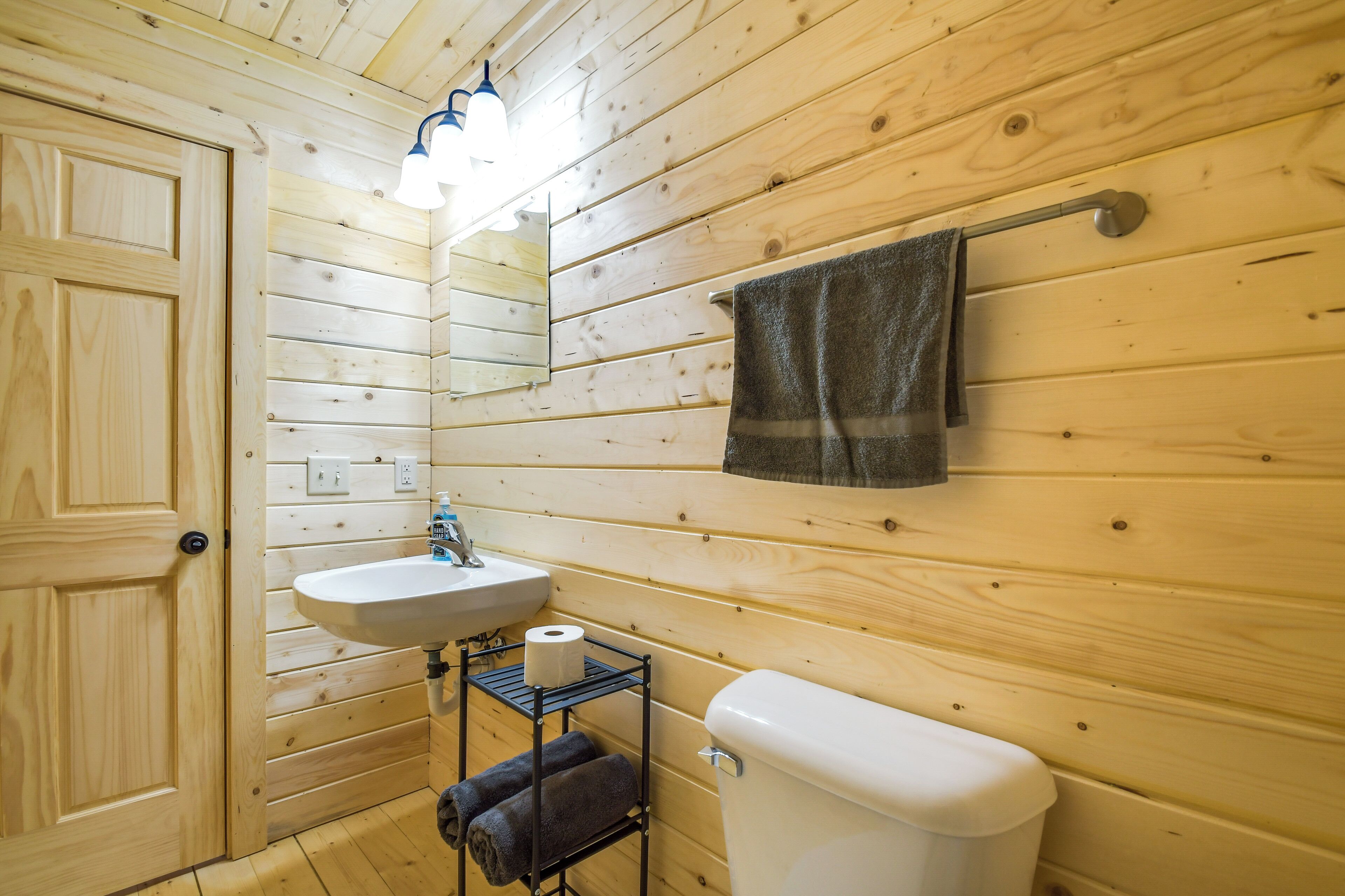 Une salle de bain aux murs lambrissés, équipée d’un lavabo, de toilettes et d’un porte-serviettes.