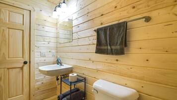 Une salle de bain aux murs lambrissés, équipée d’un lavabo, de toilettes et d’un porte-serviettes.