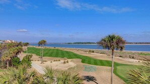 Un campo da golf con vista sull'oceano, circondato da palme e un cielo sereno.