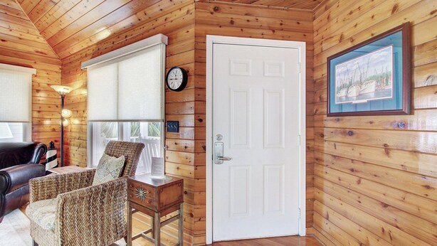 A wooden cabin interior with a white door, a clock, a framed picture, and wicker furniture. - 54 Pelican Bay by Avantstay Steps From Beach + Community Pool (Isle of Palms)