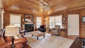 A cozy log cabin interior with a fireplace, leather furniture, and a ceiling fan. - 54 Pelican Bay by Avantstay Steps From Beach + Community Pool (Isle of Palms)