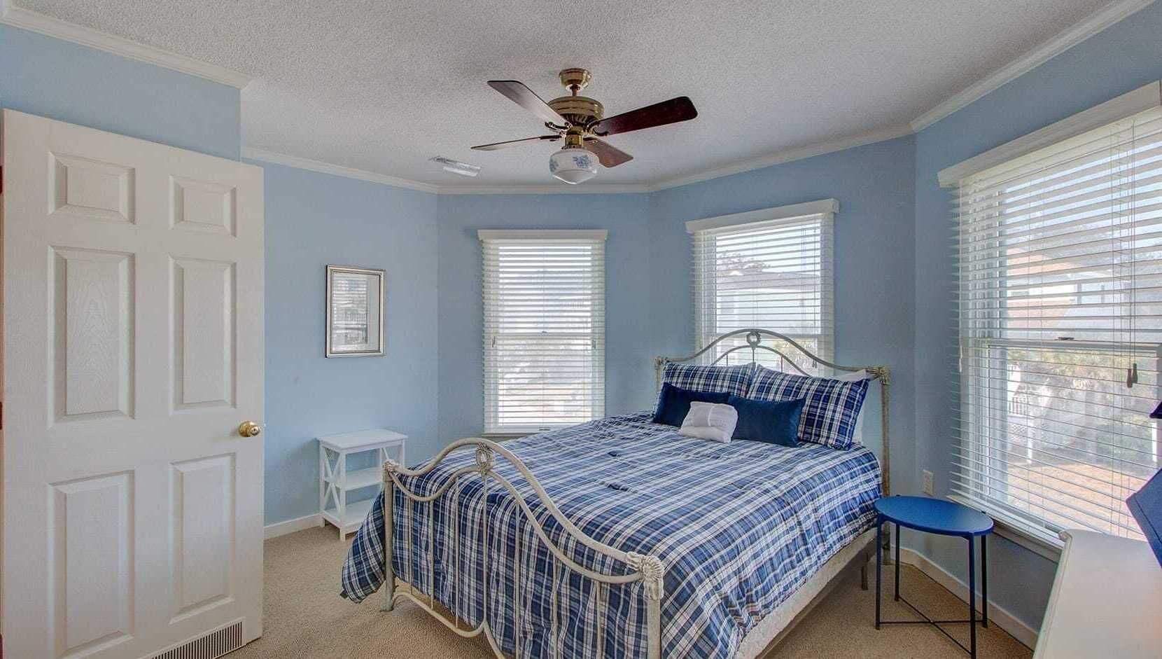 Een slaapkamer met een bed, een stoel, een plafondventilator en een raam met jaloezieën.
