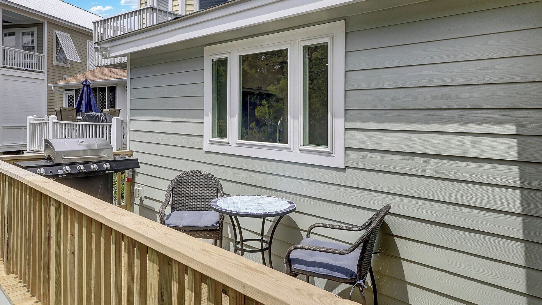A deck with a grill, two wicker chairs, and a small round table.