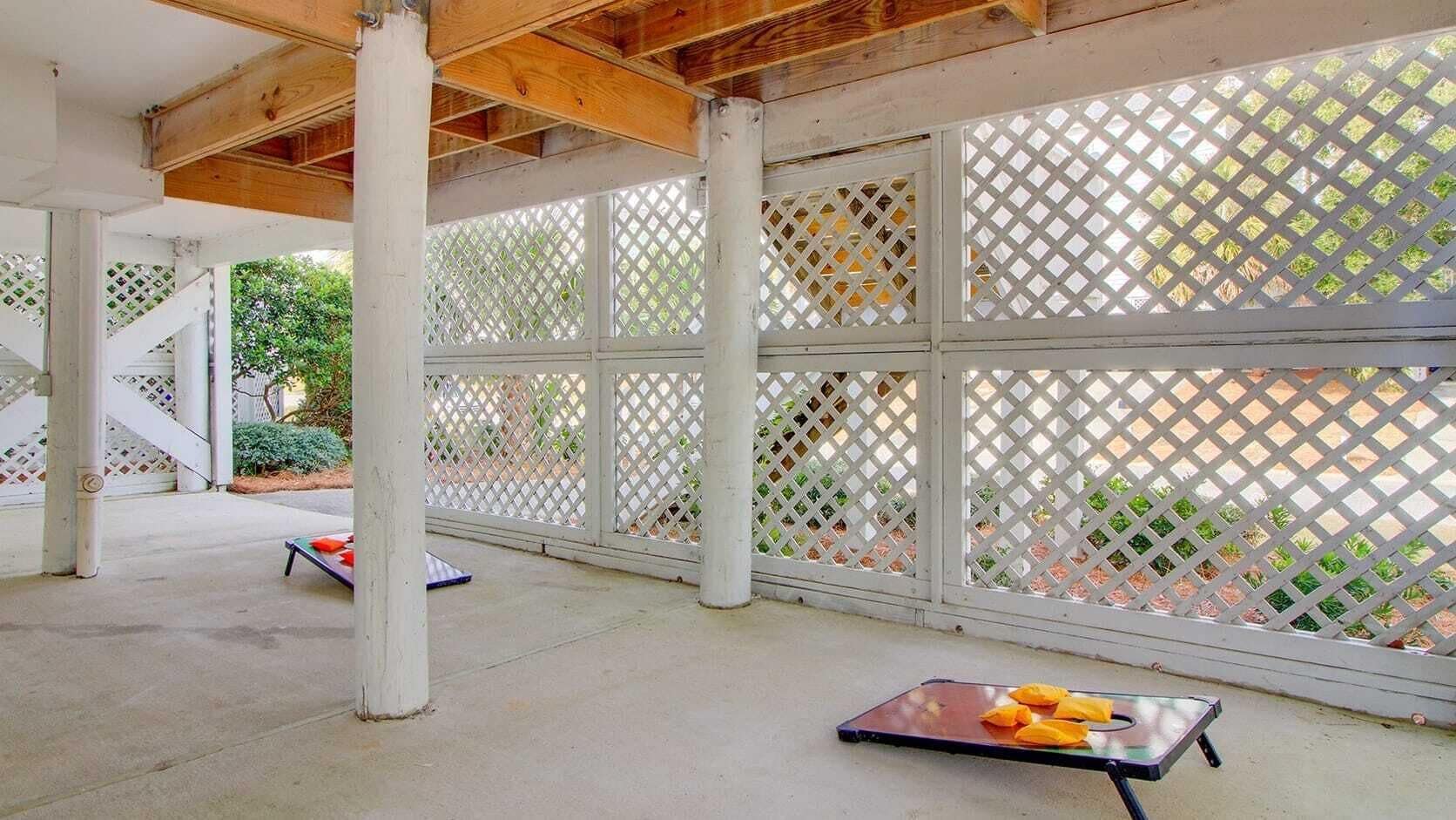 An indoor covered patio area with a concrete floor, white lattice panels, and wooden beams.