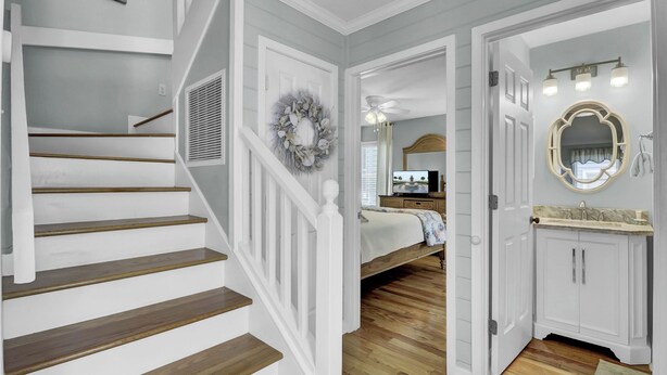Eine Treppe mit weißen Geländern und Holzstufen, ein Schlafzimmer mit Bett und Fernseher sowie ein Badezimmer mit Waschtisch und Spiegel.