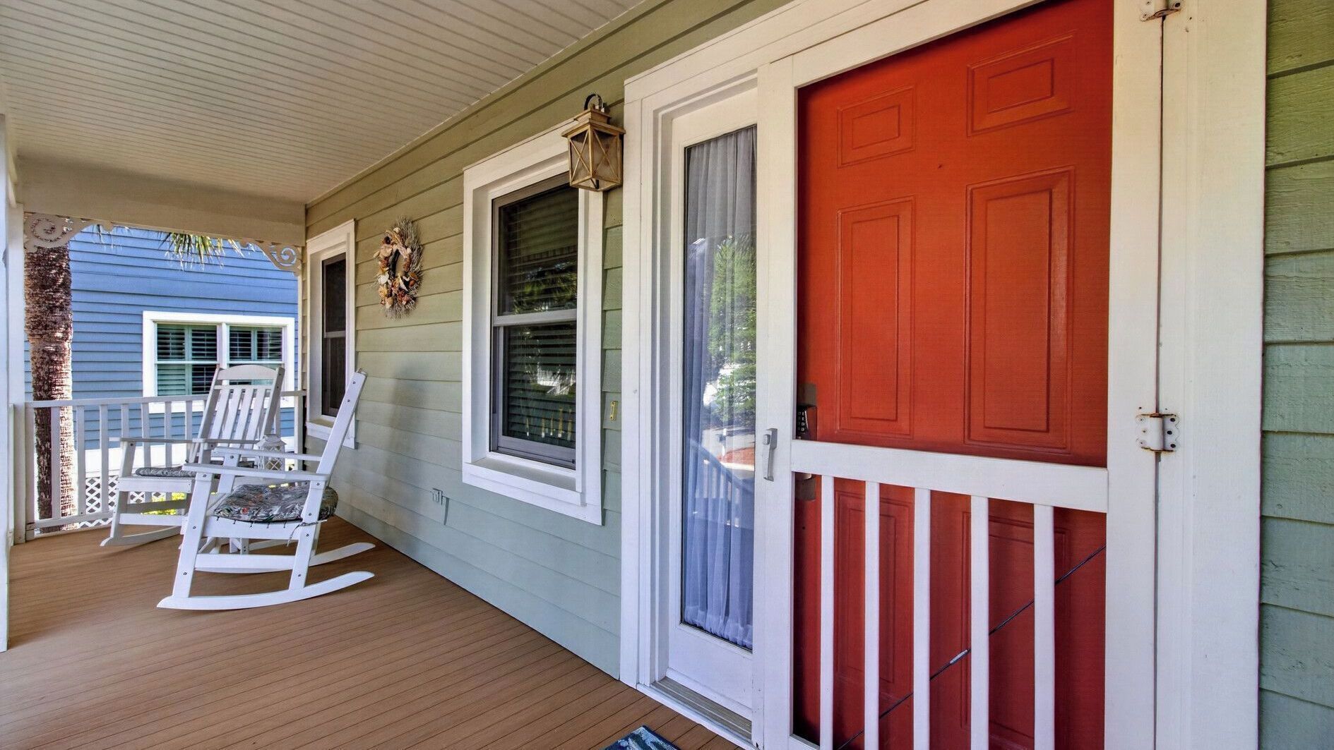 A porch with rocking chairs, a red door, and a window with a curtain.