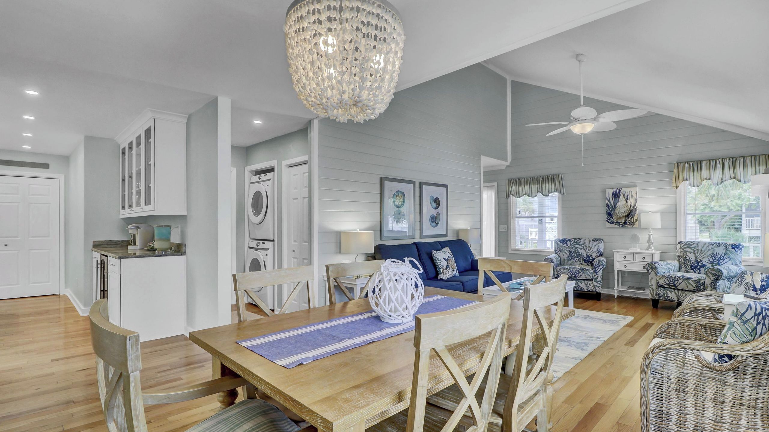 A spacious living area with a dining table, chairs, a chandelier, and a ceiling fan.