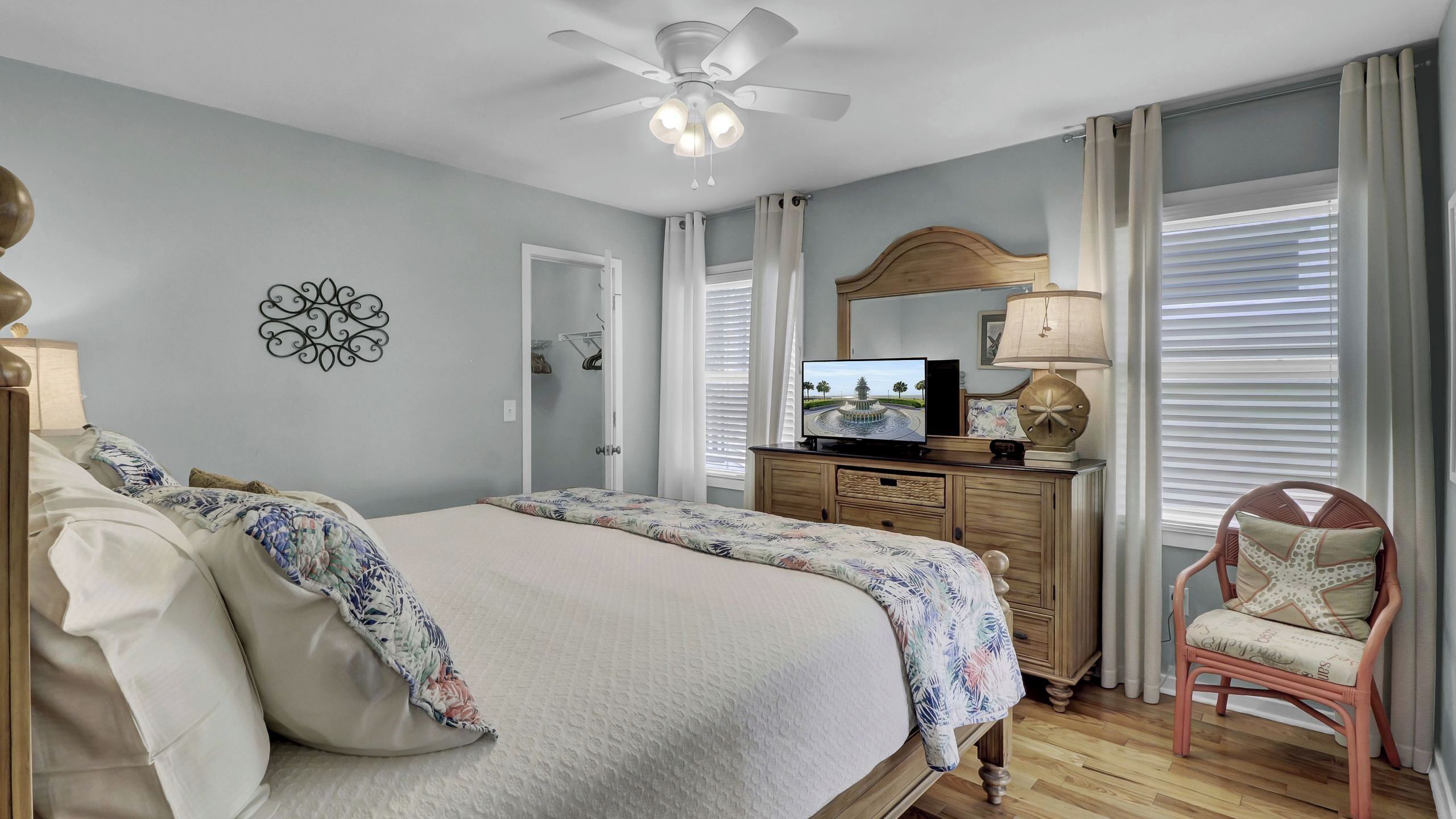 A bedroom with a bed, a television, a chair, a desk, and a ceiling fan.