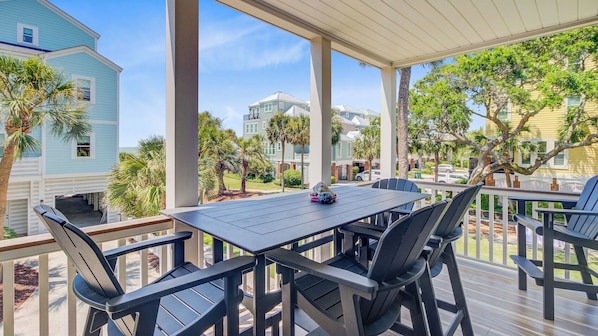 A covered outdoor patio with a table and chairs, overlooking a residential area with houses and palm trees.