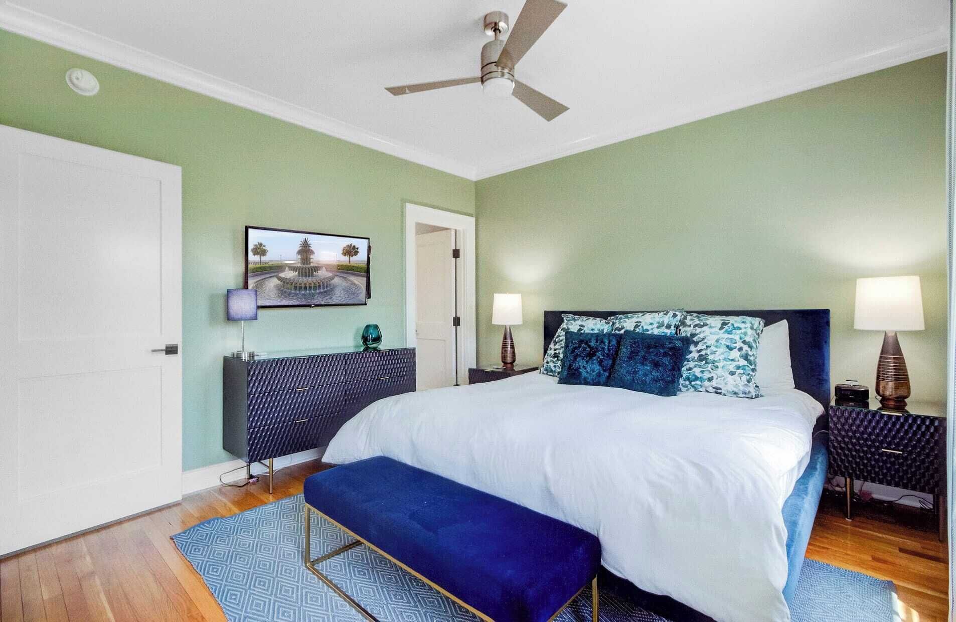 Ein Schlafzimmer mit einem Bett, einer Bank, einem Deckenventilator, einem Fernseher und zwei Nachttischen mit Lampen.
