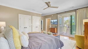 A bedroom with a bed, a ceiling fan, a TV, and a sliding glass door to a balcony.