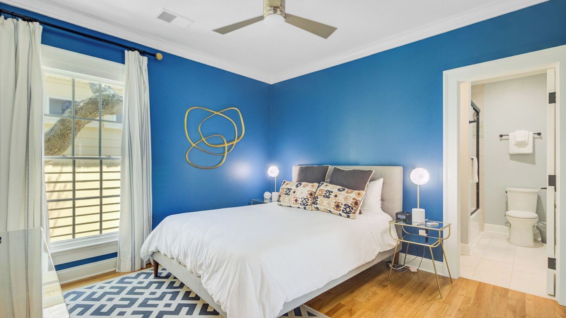 A bedroom with a bed, bedside lamps, a ceiling fan, and a window with curtains.