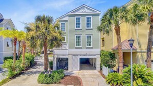 A two-story building with a garage entrance, surrounded by palm trees and a well-maintained garden. - 56 Grand Pavilion by Avantstay Oceanfront Deck + Views, Community Pool (Isle of Palms)