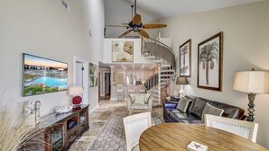 A spacious living area with a high ceiling, a central staircase, and a dining table. - 519 Seascape by Avantstay Shared Pool + Views, Incredible Interior Design (Isle of Palms)