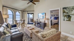A spacious living room with a large window overlooking the beach, a ceiling fan, and a dining area with a view. - 519 Seascape by Avantstay Shared Pool + Views, Incredible Interior Design (Isle of Palms)
