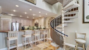 A kitchen with a central island, bar stools, and a spiral staircase. - 519 Seascape by Avantstay Shared Pool + Views, Incredible Interior Design (Isle of Palms)