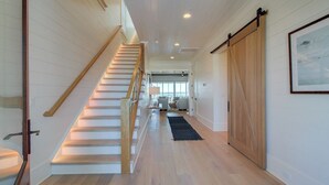 A staircase with wooden railings leading to a second floor, a sliding barn-style door, and a framed picture on the wall. - 710 Ocean Boulevard Avantstay Oceanfront, Private Pool + Rooftop Deck (Isle of Palms)