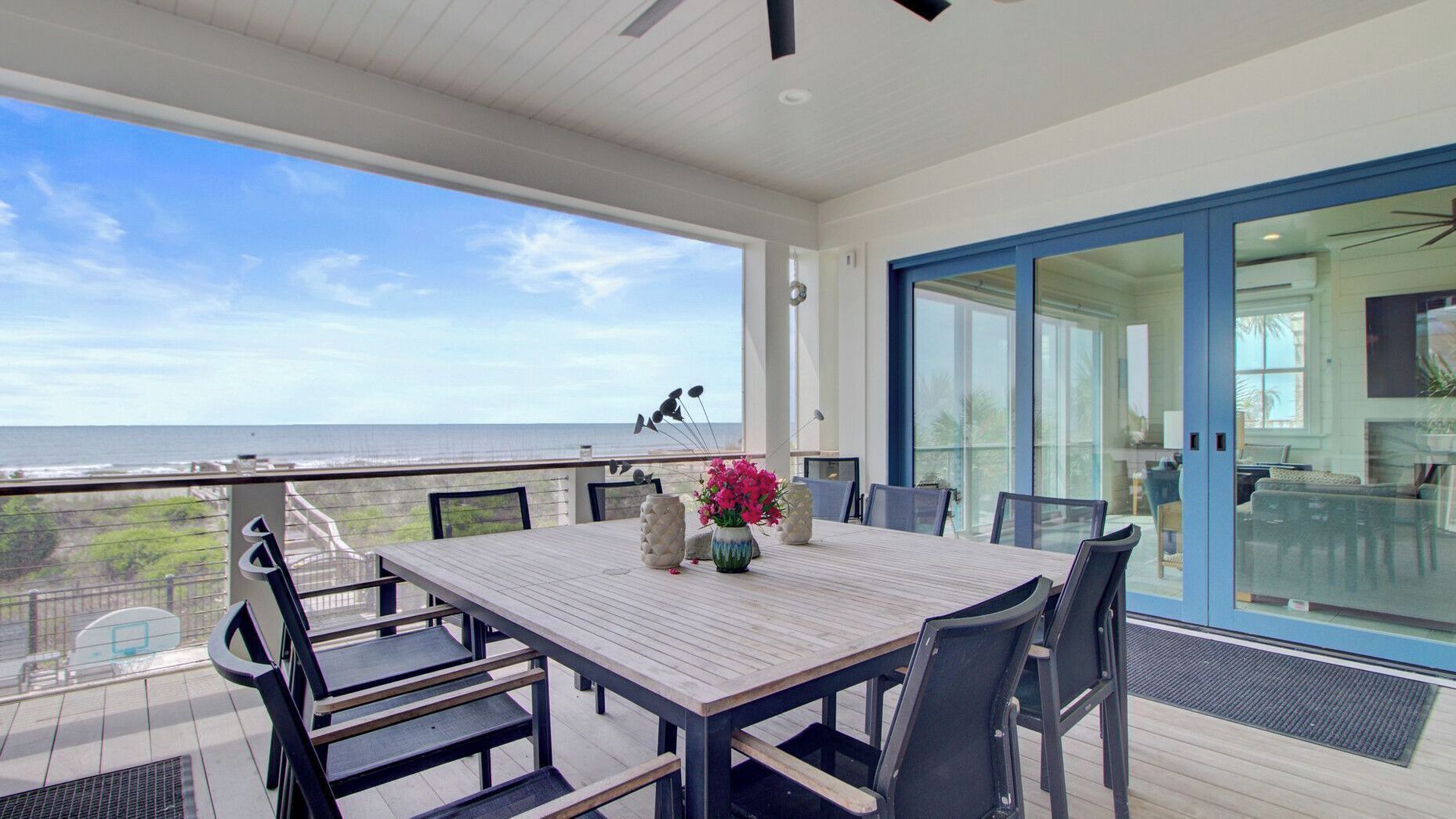 A balcony with a table and chairs, overlooking a beach and ocean.
