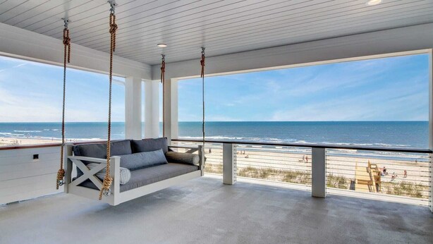 A spacious balcony with a swing chair overlooking a beach. - 710 Ocean Boulevard Avantstay Oceanfront, Private Pool + Rooftop Deck (Isle of Palms)