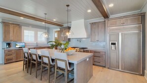 A modern kitchen with wooden cabinets, a central island with bar stools, pendant lighting, and a built-in oven. - 710 Ocean Boulevard Avantstay Oceanfront, Private Pool + Rooftop Deck (Isle of Palms)