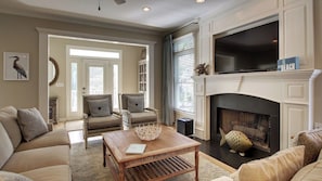 A living room with a fireplace, two armchairs, a coffee table, and a television.