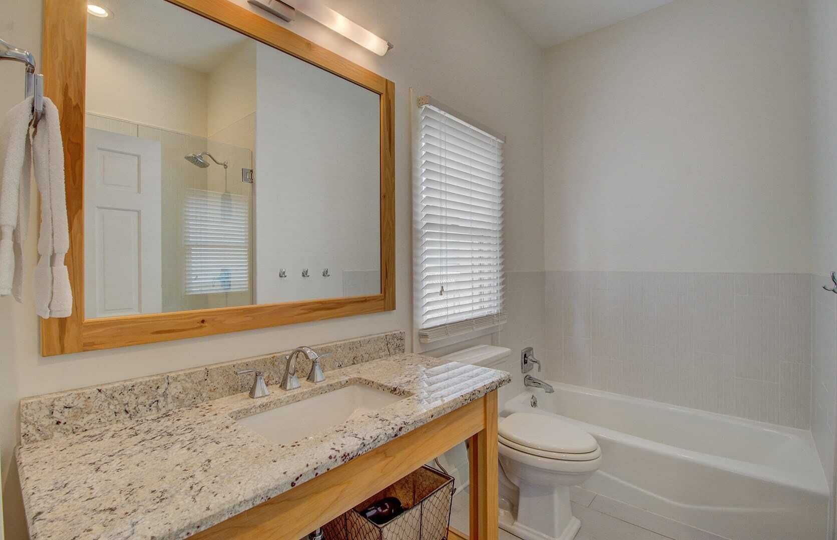 Une salle de bain avec un comptoir en granit, un meuble-lavabo en bois, des toilettes blanches et une baignoire.
