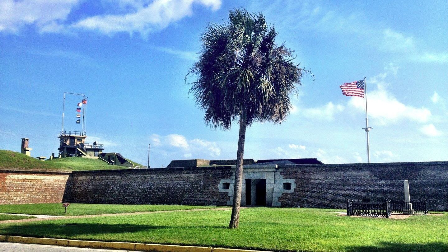 A fortified structure with a palm tree, American flags, and a clear sky.