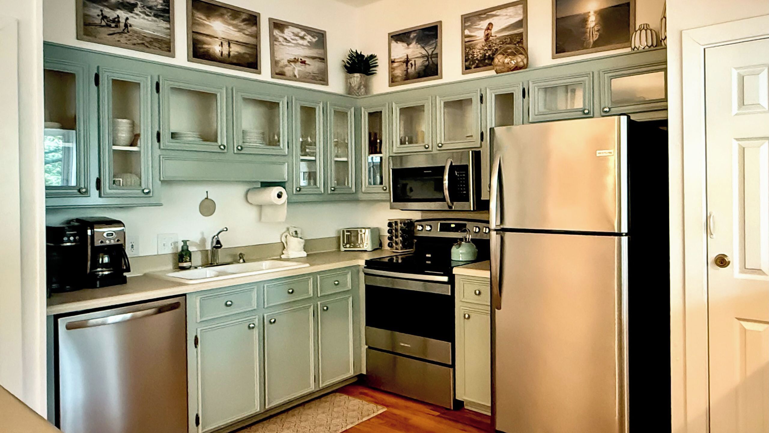A kitchen with light blue cabinets, a stainless steel refrigerator, a microwave, a toaster, and a coffee maker.