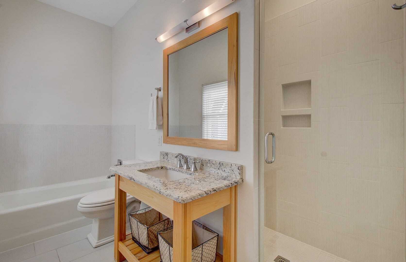 Un baño con una bañera blanca, un tocador de madera con encimera de mármol, un espejo grande y un perchero para toallas.