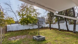 Un patio trasero con una jardinera de hormigón, una valla blanca y árboles.