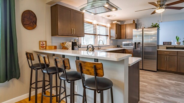 Una cocina moderna con una isla central, taburetes de bar, electrodomésticos de acero inoxidable y armarios de madera.