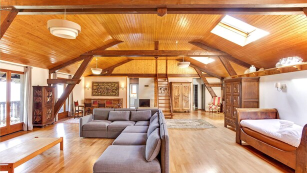 A spacious loft with wooden beams, a sectional sofa, a bed, and a dining area.