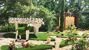 Un jardin agrémenté d’un banc orné de mosaïques, d’une statue et d’une fontaine.