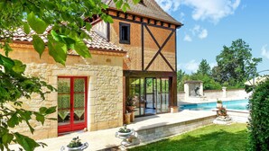 Une maison traditionnelle à colombages, avec une façade en pierre, une porte rouge et une piscine dans le jardin.
