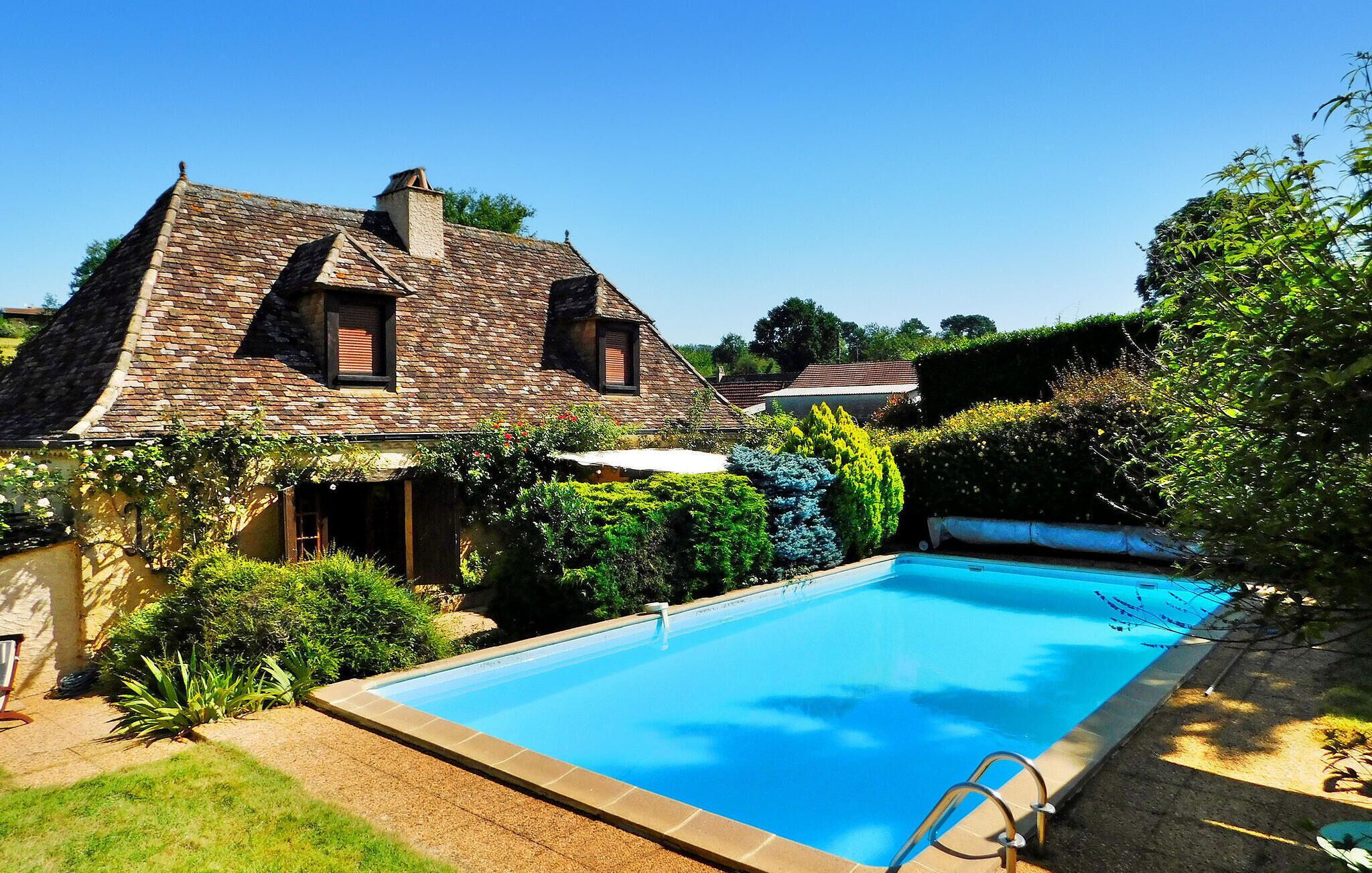 A traditional house with a stone roof, a swimming pool, and lush greenery.
