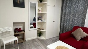 Un saló modern amb un sofà blanc, un armari vermell, una taula de cafè blanca i una cadira blanca. Hi ha un moble blanc amb prestatges, una taula petita amb una bossa vermella i un quadre a la paret.