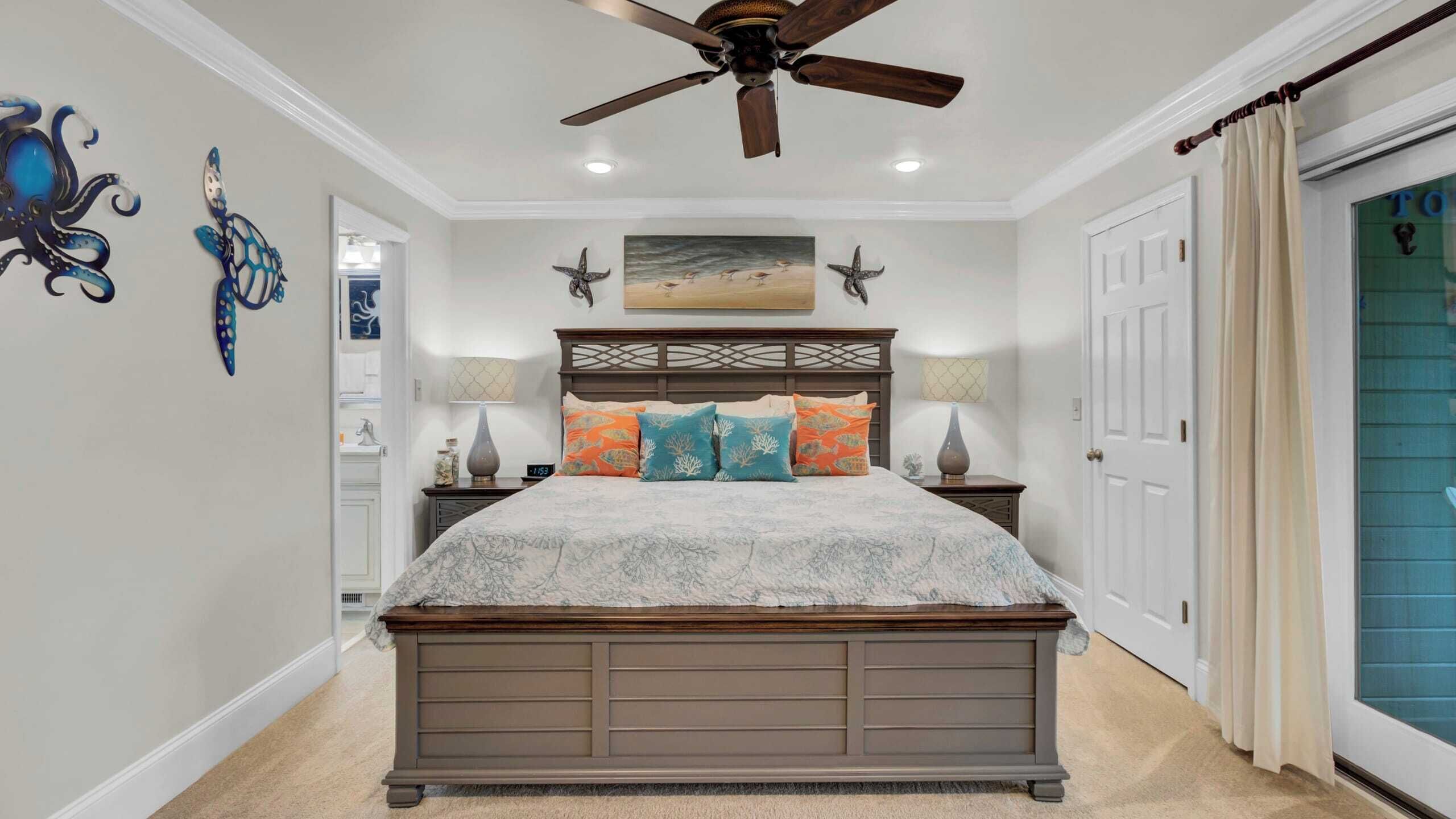 A bedroom with a large bed, a ceiling fan, and artwork on the walls.