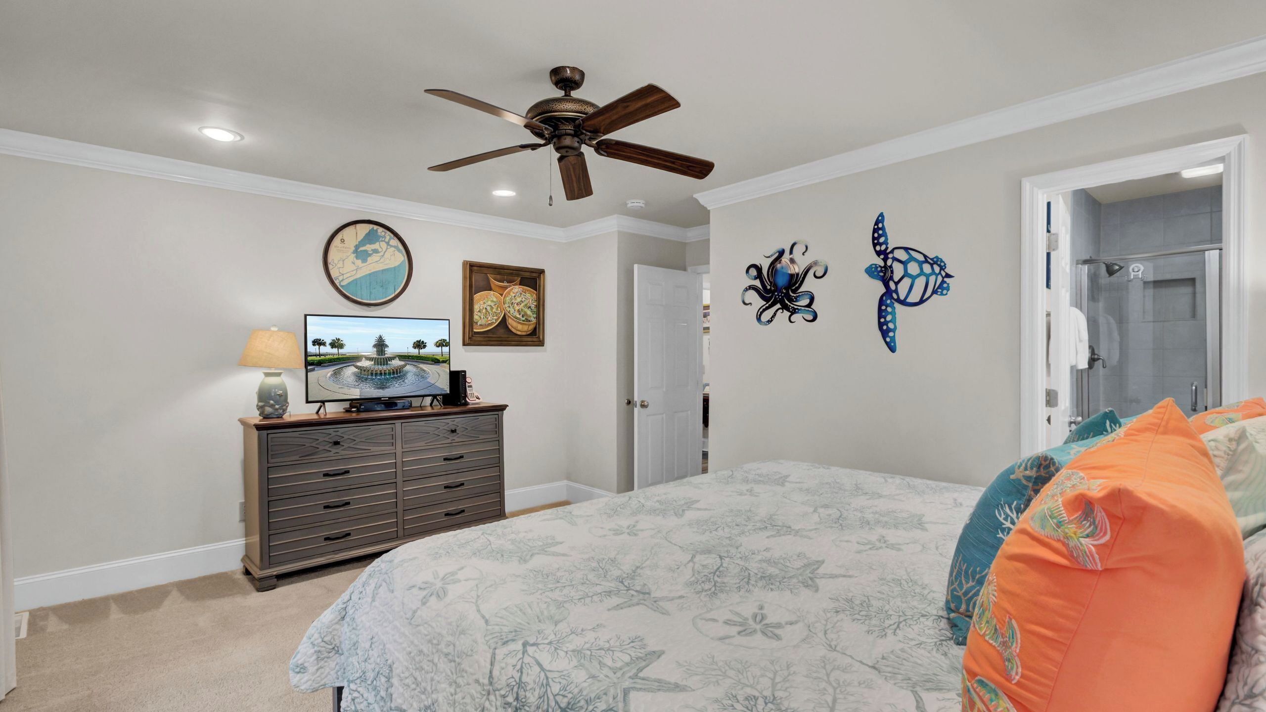 A bedroom with a bed, dresser, ceiling fan, wall art, and a door leading to another room.
