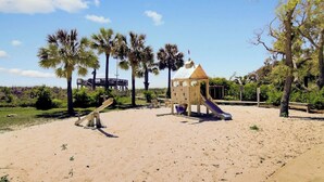 A sandy playground with a wooden slide and swings, surrounded by palm trees. - 121 D Shipwatch by Avantstay Oceanfront Villa w/ View (Isle of Palms)