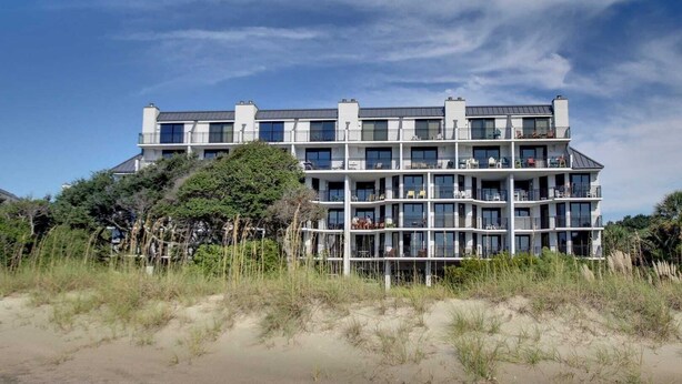 A multi-story hotel with balconies, located near a beach with sand dunes and vegetation. - 121 D Shipwatch by Avantstay Oceanfront Villa w/ View (Isle of Palms)