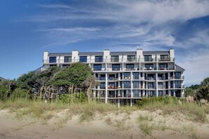 A multi-story hotel with balconies, located near a beach with sand dunes and vegetation. - 121 D Shipwatch by Avantstay Oceanfront Villa w/ View (Isle of Palms)