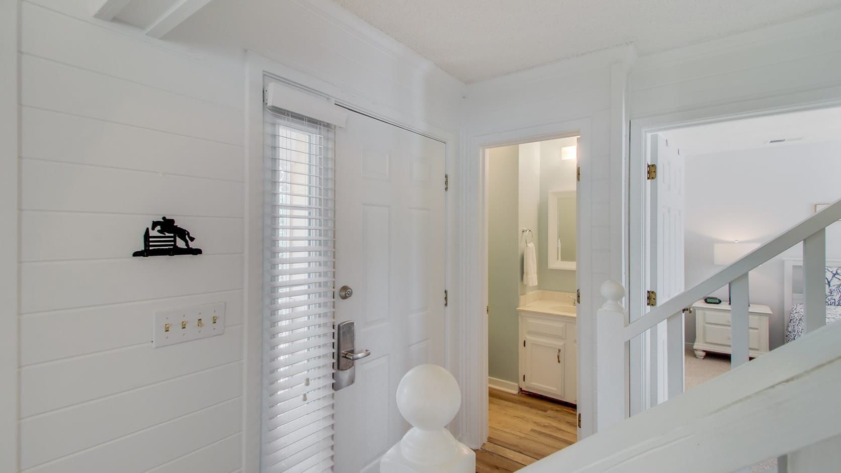 A hallway with white walls, a door with a metal handle, and a white statue.