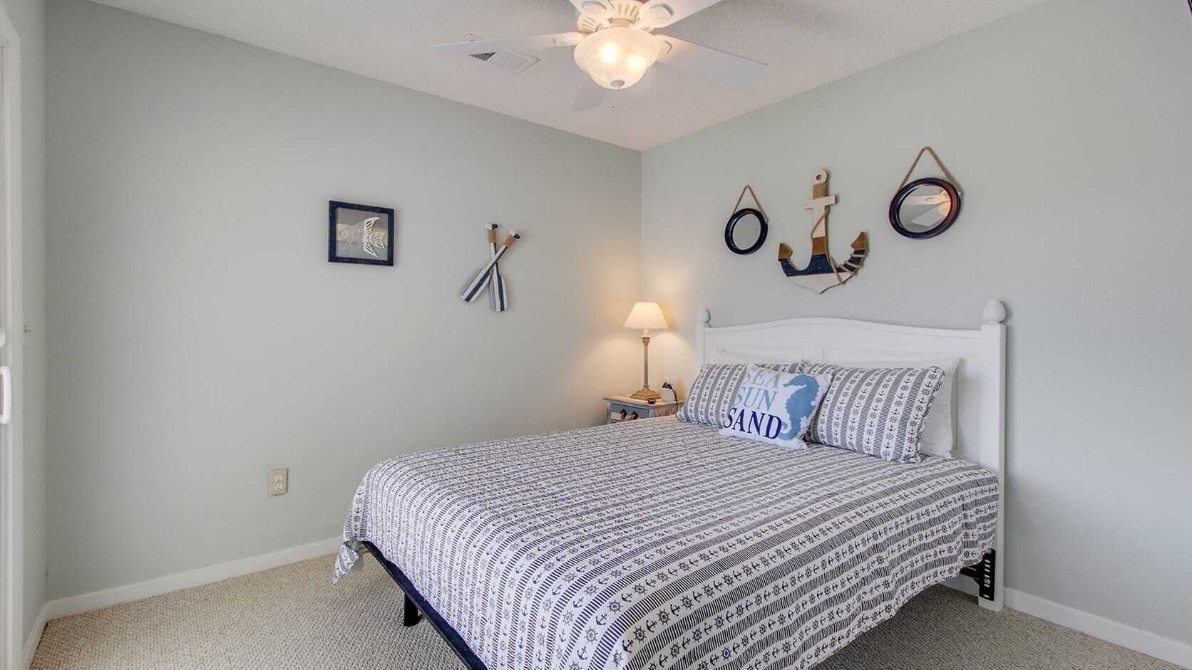 Een slaapkamer met een bed, nachtkastje, lamp en muurdecoraties met een nautisch thema.