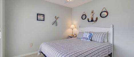 A bedroom with a bed, a nightstand, a lamp, and nautical-themed wall decorations.