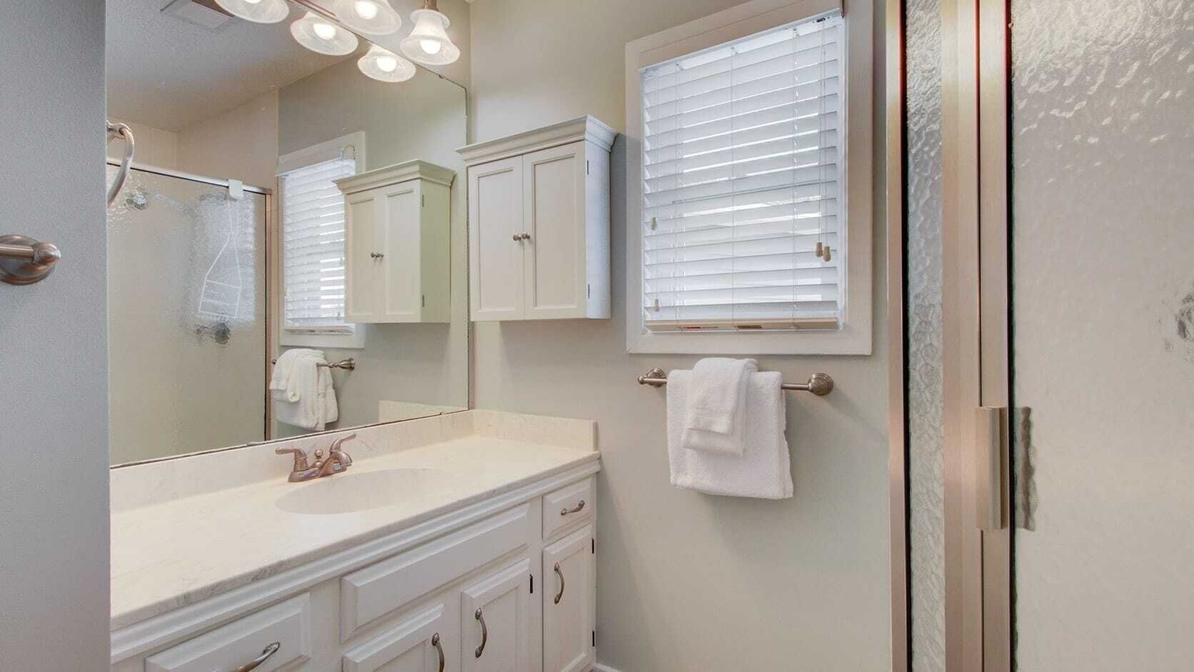 Un baño con tocador, espejo, perchero y una ventana con persianas.