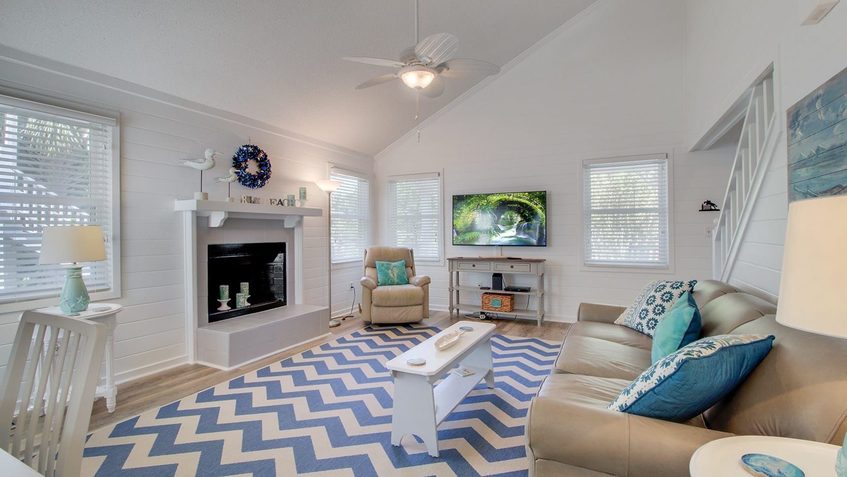 A living room with a fireplace, a television, a ceiling fan, and a patterned rug.
