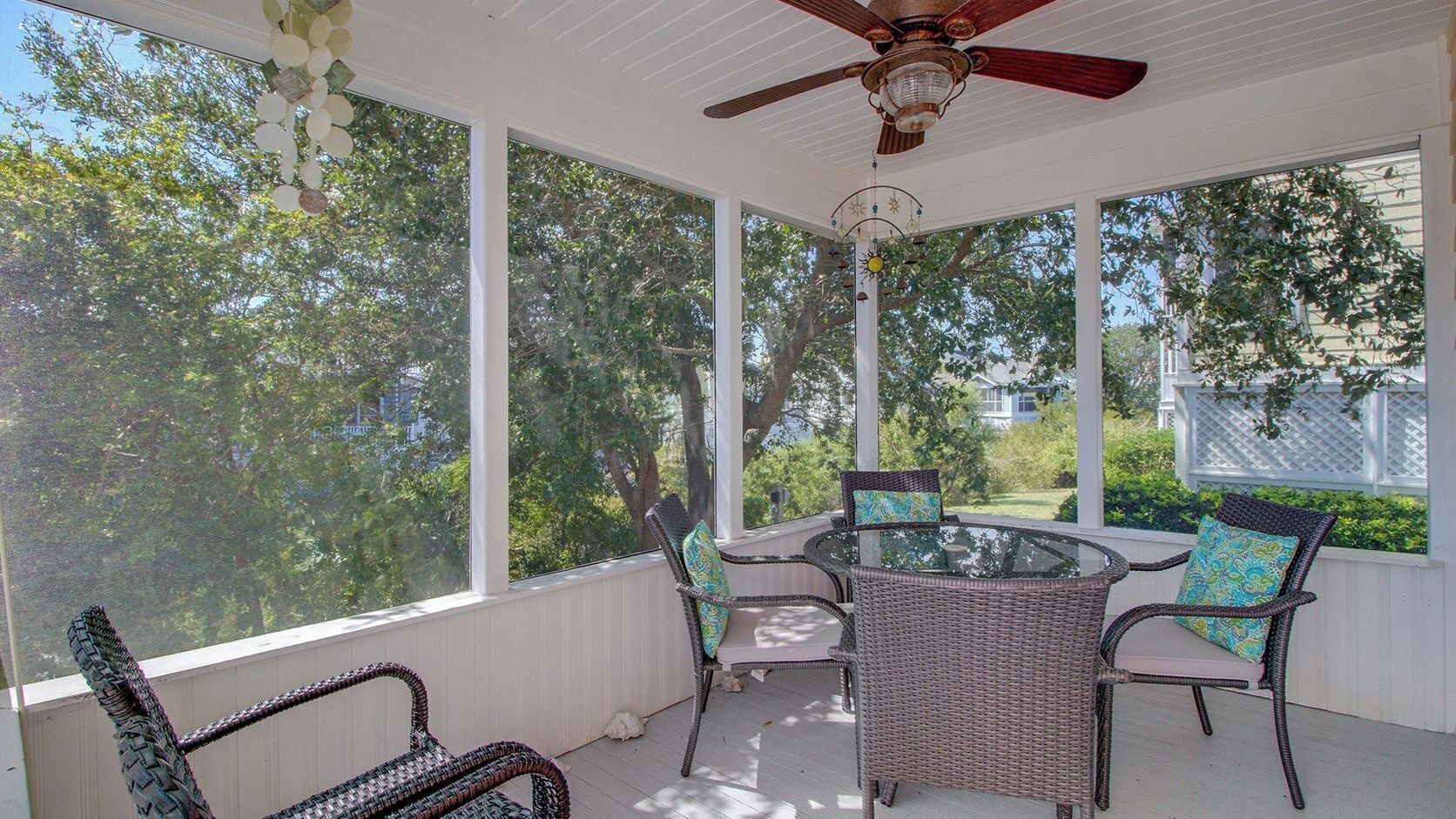 A covered patio with wicker furniture, a glass table, and a ceiling fan.
